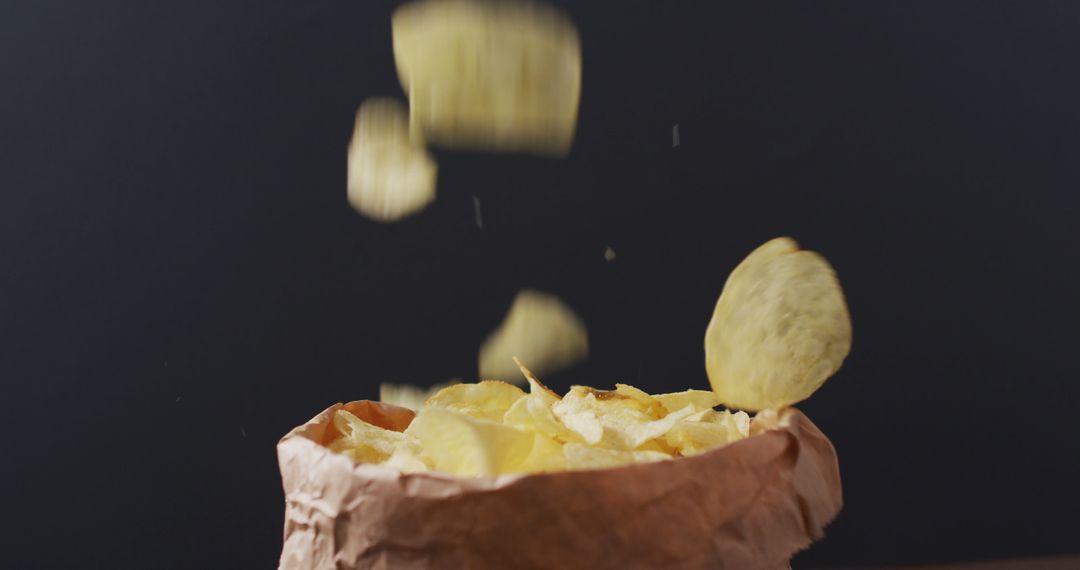 Close up view of potato chips falling in a paper bag against black background - Free Images, Stock Photos and Pictures on Pikwizard.com