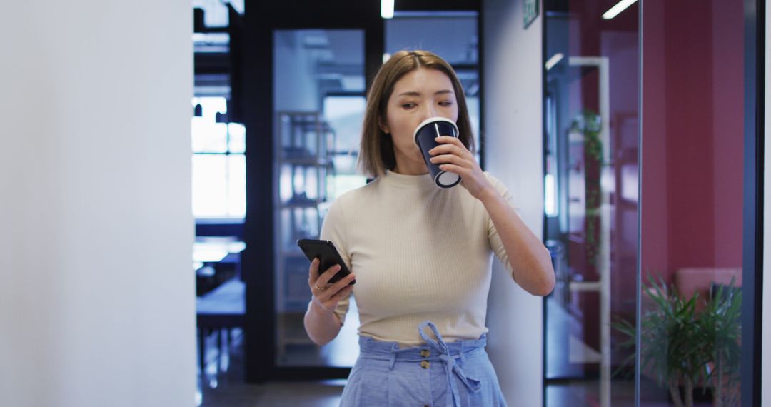 Young Woman Walking and Drinking Coffee in Modern Office - Free Images, Stock Photos and Pictures on Pikwizard.com