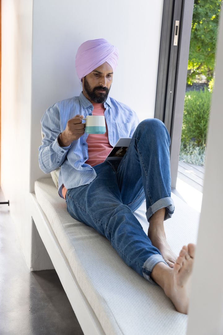 Man in Turban Relaxing by Window with Tablet and Coffee Mug