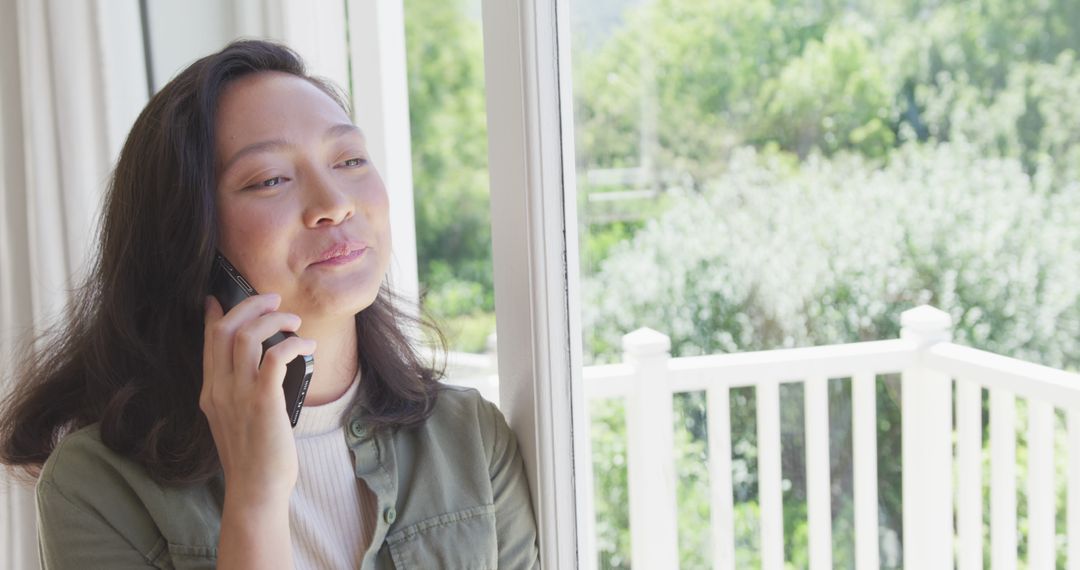 Woman Happily Talking Phone by Window in Sunny Home - Free Images, Stock Photos and Pictures on Pikwizard.com