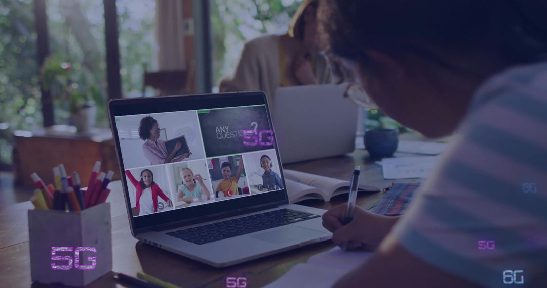 Child attending virtual classroom on laptop while writing homework at home workspace