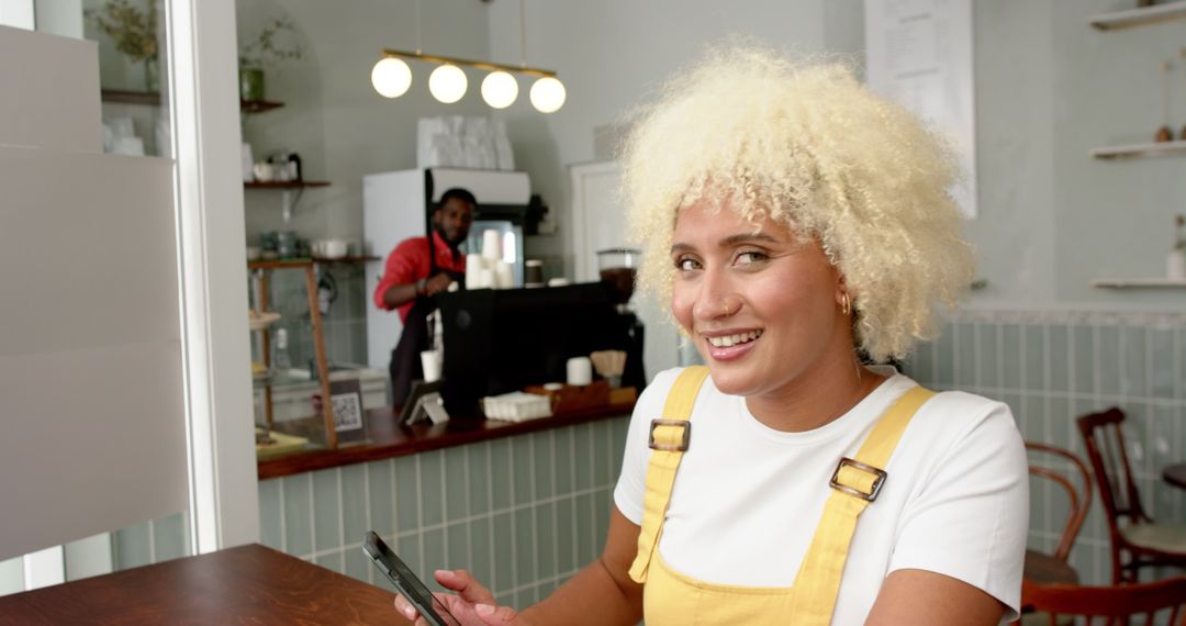 Woman Relaxing in Cafe using Smartphone Smiling at Camera