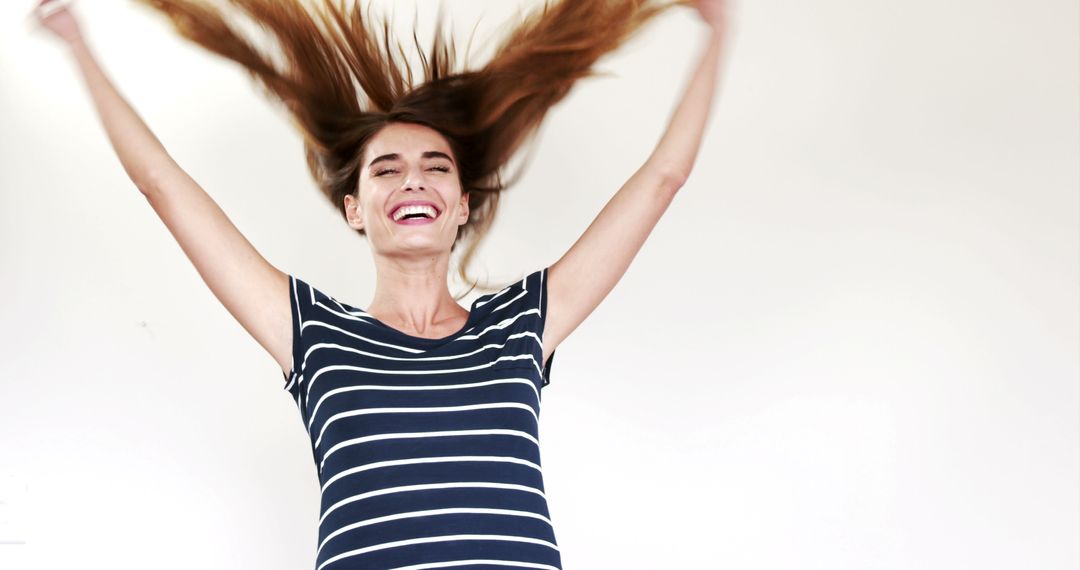 Joyful Woman with Long Hair Smiling and Jumping in Striped T-shirt - Free Images, Stock Photos and Pictures on Pikwizard.com