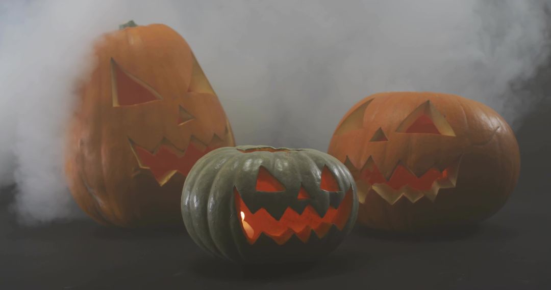 Glowing carved jack-o'-lanterns sitting on dark table with drifting fog