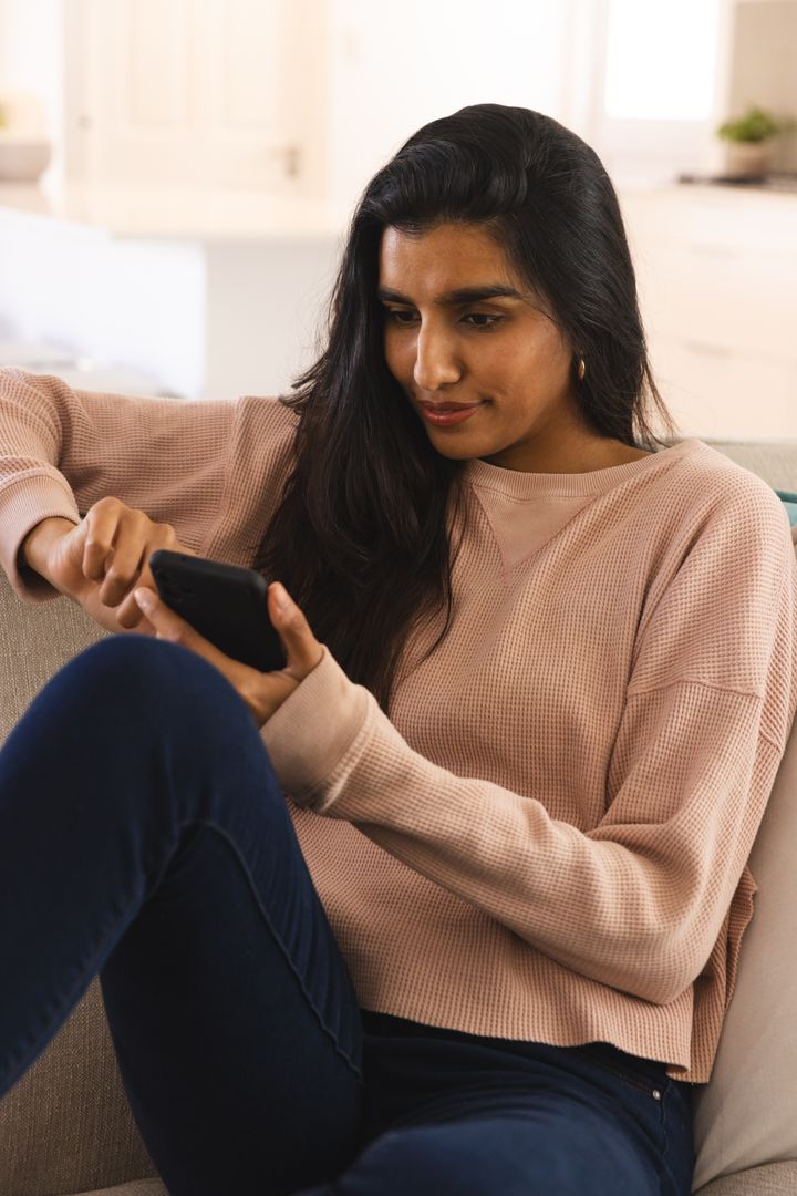 Asian Woman Relaxing on Sofa Using Smartphone in Cozy Living Room