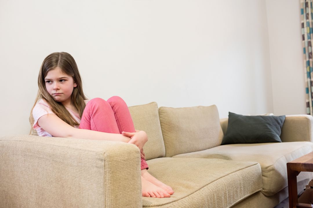 Contemplative Child Hugging Knees on Sofa at Home