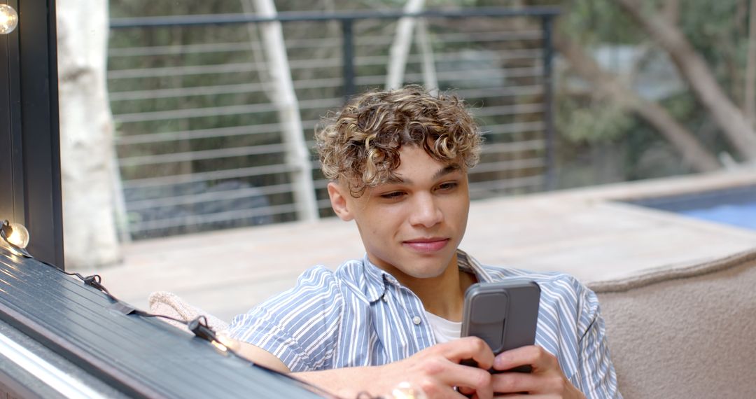 Young Man Relaxing with Smartphone Outdoors under String Lights