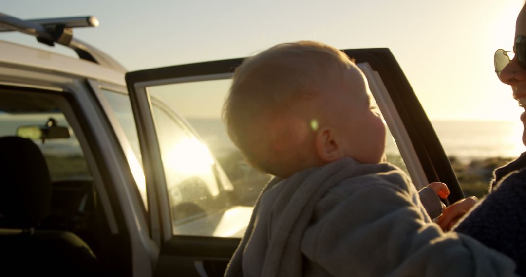 Mother holding baby outdoors by car during sunset - Free Images, Stock Photos and Pictures on Pikwizard.com