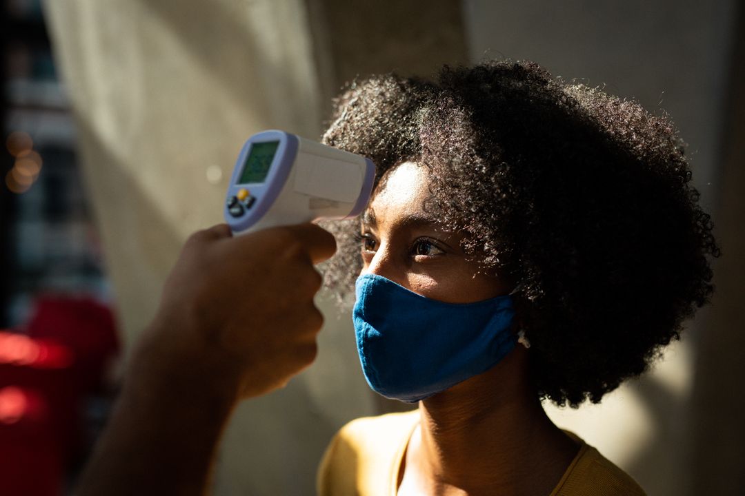 African american woman wearing face mask having temperature taken by colleague before work - Free Images, Stock Photos and Pictures on Pikwizard.com