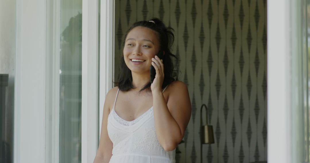 Smiling Woman Talking on Smartphone Steps Away from Window