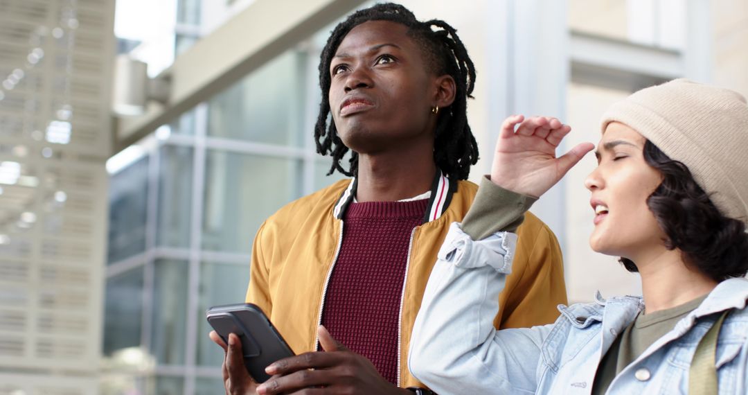 Diverse friends navigating modern transit hub holding smartphone and looking up