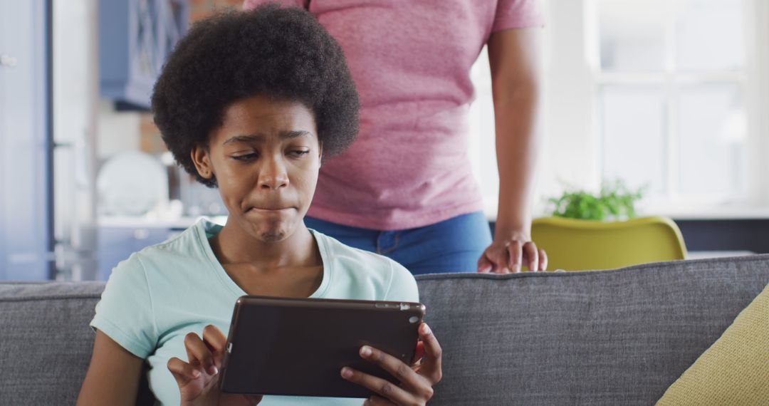 Teenager Using Digital Tablet on Couch While Adult Observes in Background - Free Images, Stock Photos and Pictures on Pikwizard.com