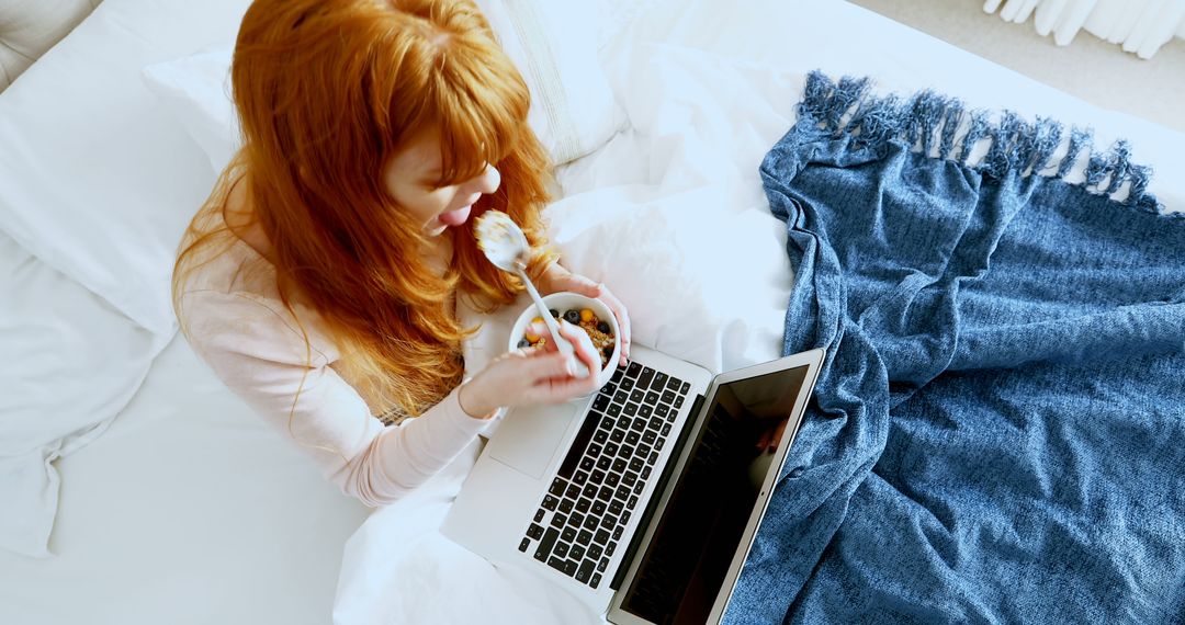 Young Woman Watching Laptop and Eating Breakfast in Bed - Free Images, Stock Photos and Pictures on Pikwizard.com