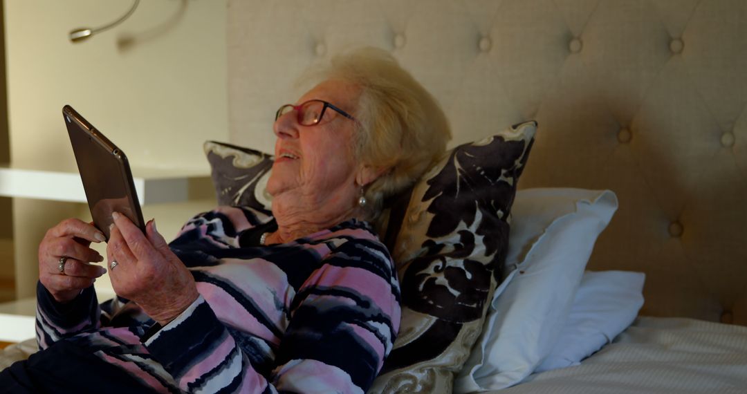 Elderly woman relaxing in bed while using tablet - Free Images, Stock Photos and Pictures on Pikwizard.com