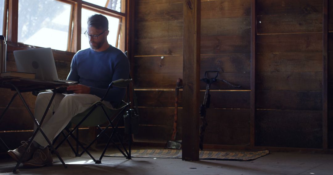 Man Working on Laptop in Rustic Cabin with Wooden Walls - Free Images, Stock Photos and Pictures on Pikwizard.com