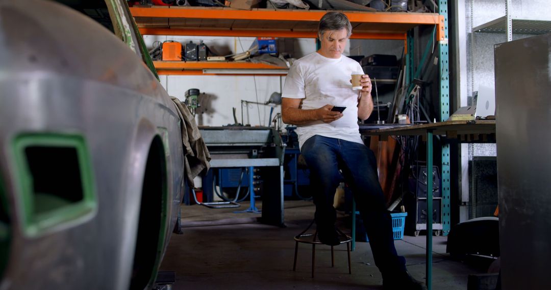 Man Relaxing with Coffee at Workbench in Automotive Garage - Free Images, Stock Photos and Pictures on Pikwizard.com