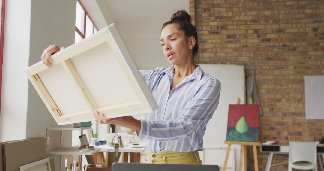 Image of happy biracial female artist looking at painting in studio - Free Images, Stock Photos and Pictures on Pikwizard.com