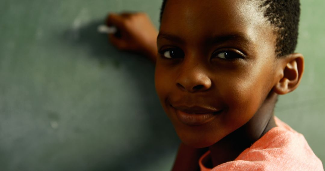 Smiling African American Boy Writing on Chalkboard in Classroom
