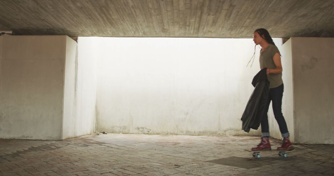 Woman Skateboarding Under Concrete Structure Holding Jacket - Free Images, Stock Photos and Pictures on Pikwizard.com