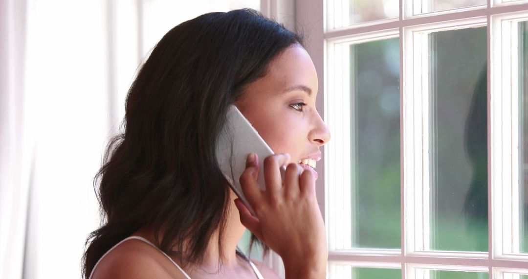 Young Woman Talking on Smartphone by Window with Natural Light - Free Images, Stock Photos and Pictures on Pikwizard.com