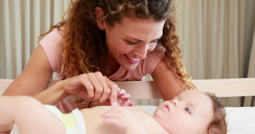 Mother Smiling While Changing Baby's Diaper in Nursery - Free Images, Stock Photos and Pictures on Pikwizard.com