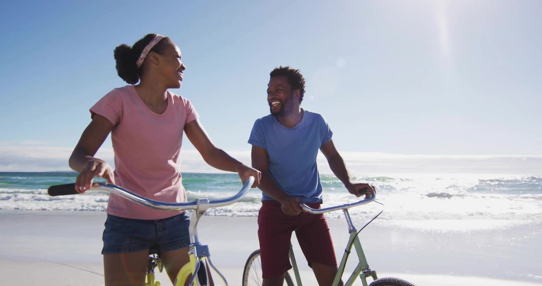 Joyful Couple Walking Bicycles on Sunlit Beach