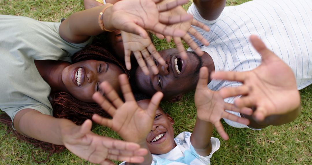 Happy Family Lying on Grass Reaching Toward Camera