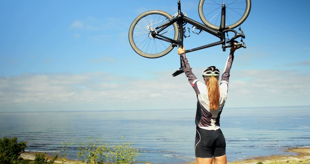 Cyclist Celebrating Triumph by Raising Bicycle by Scenic Beach - Free Images, Stock Photos and Pictures on Pikwizard.com