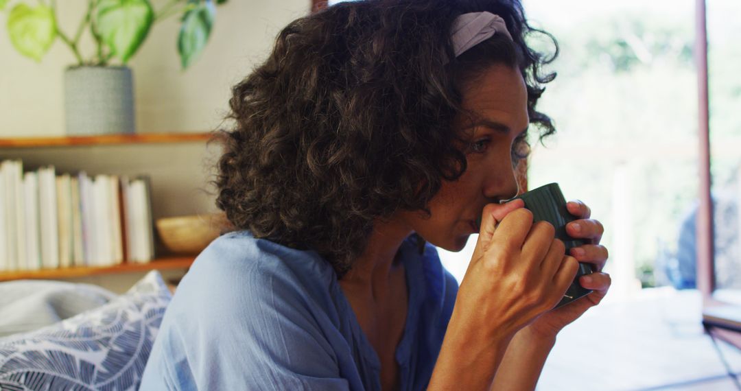 Biracial woman drinking coffee while sitting on the couch at home - Free Images, Stock Photos and Pictures on Pikwizard.com