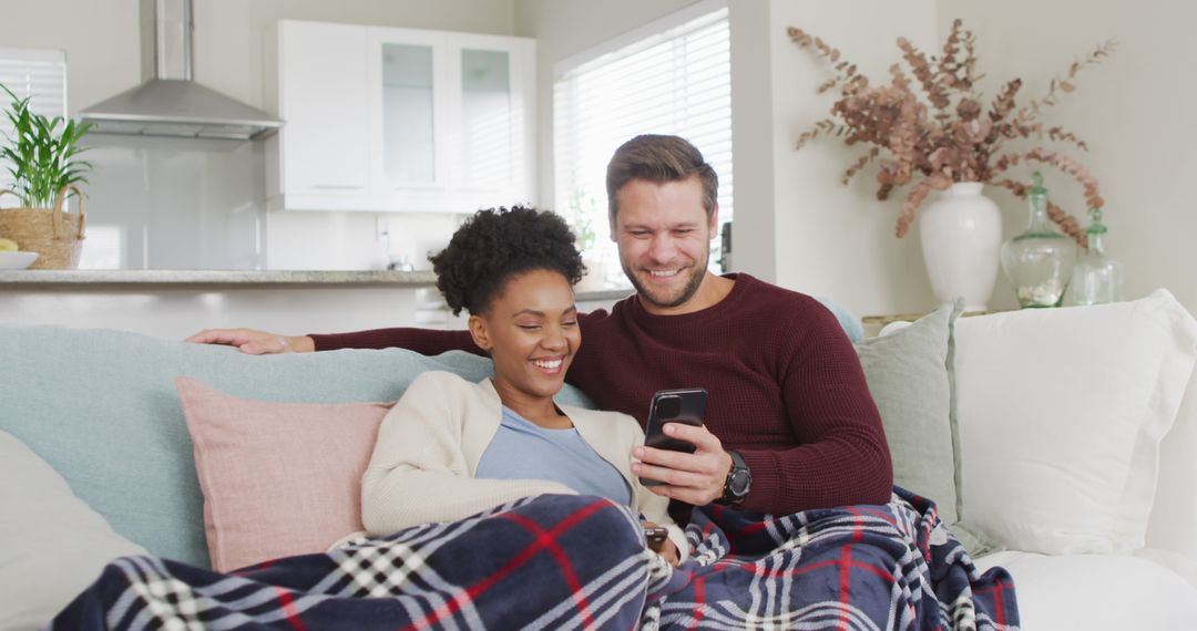Image of happy diverse couple embracing and using smartphone on sofa - Free Images, Stock Photos and Pictures on Pikwizard.com