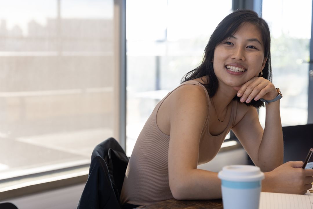 Smiling Woman Sitting by Window with Smartphone and Coffee