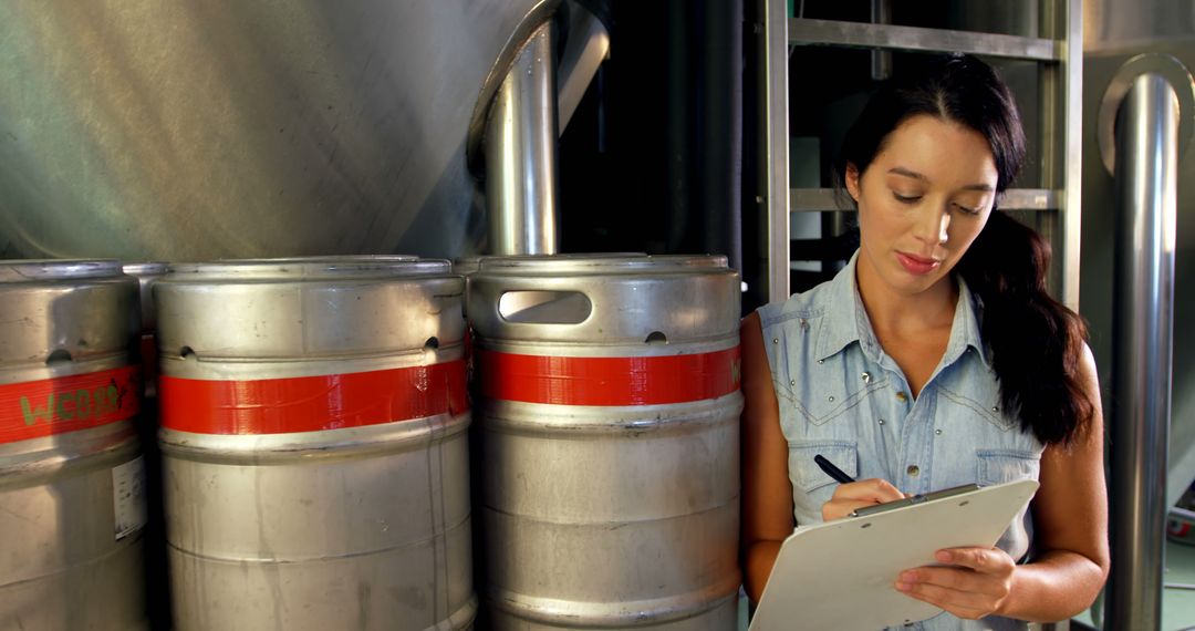 Female Brewery Worker Inspecting Beer Kegs with Clipboard - Free Images, Stock Photos and Pictures on Pikwizard.com