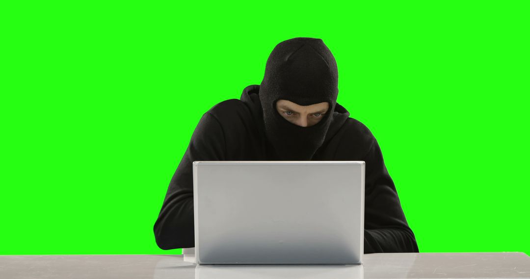 Masked Hacker Operating on Laptop with Green Background - Free Images, Stock Photos and Pictures on Pikwizard.com