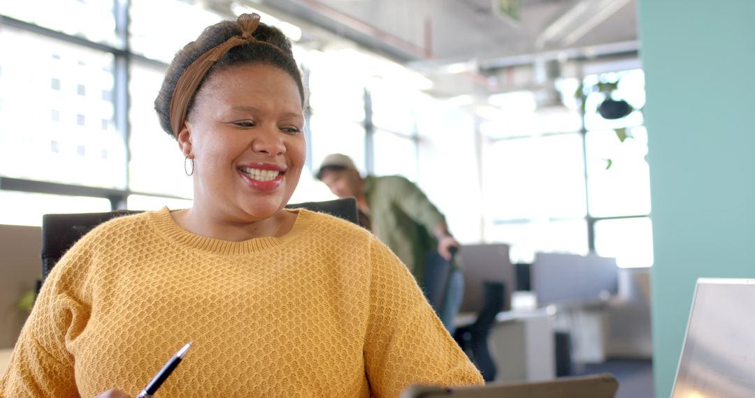 Smiling woman in mustard sweater collaborating with team in bright modern open office