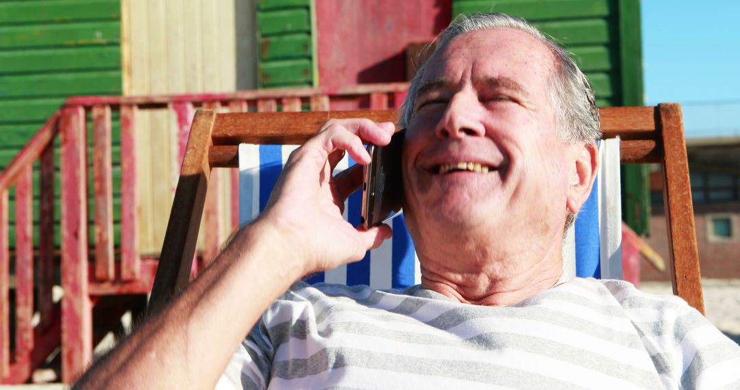 Happy Senior Man Relaxing on Deck Chair and Talking on Phone at Beach - Free Images, Stock Photos and Pictures on Pikwizard.com