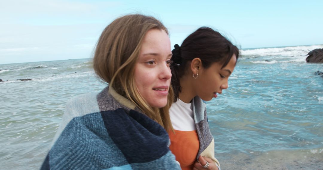 Two Young Women Enjoying Time at the Beach Wrapped in a Blanket - Free Images, Stock Photos and Pictures on Pikwizard.com