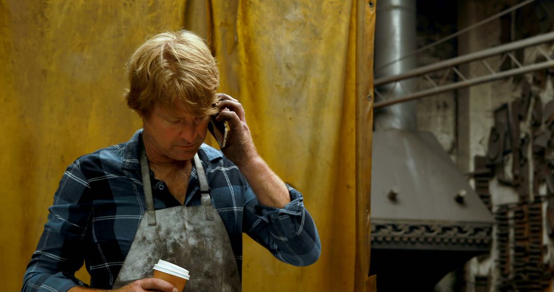 Worker on Phone Holding Coffee in Industrial Workshop - Free Images, Stock Photos and Pictures on Pikwizard.com