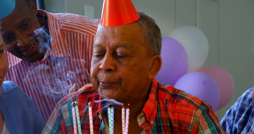 A senior man joyfully blows out birthday candles among a diverse group of celebrants. - Free Images, Stock Photos and Pictures on Pikwizard.com