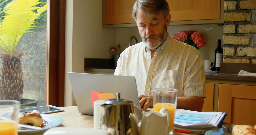 Senior man working on laptop from home with breakfast on table - Free Images, Stock Photos and Pictures on Pikwizard.com