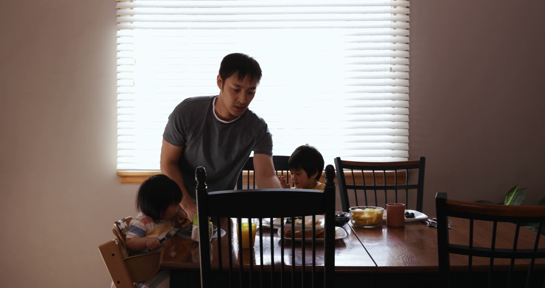 Father Feeding Young Children at Dining Table - Free Images, Stock Photos and Pictures on Pikwizard.com