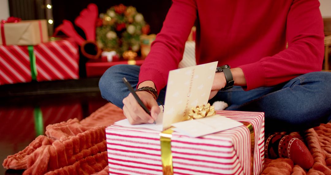 Person Writing Christmas Card with Wrapped Gift in Cozy Home - Free Images, Stock Photos and Pictures on Pikwizard.com