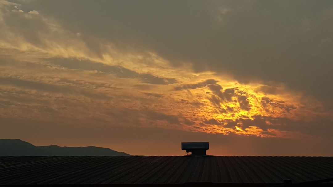 Dramatic Sunset Over Rooftop and Silhouetted Mountains - Free Images, Stock Photos and Pictures on Pikwizard.com