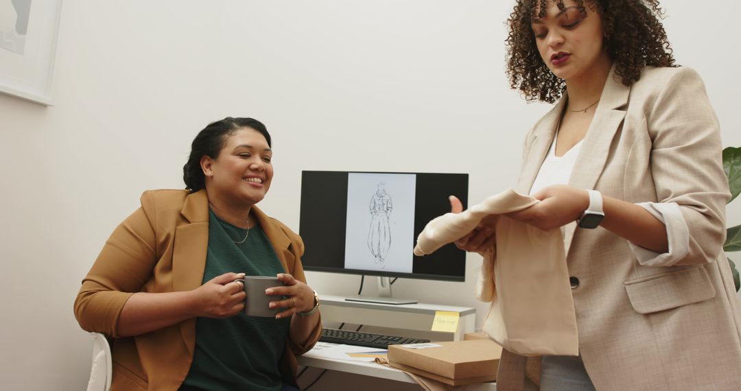 Female fashion colleagues collaborating in studio presenting beige fabric swatch and sketch