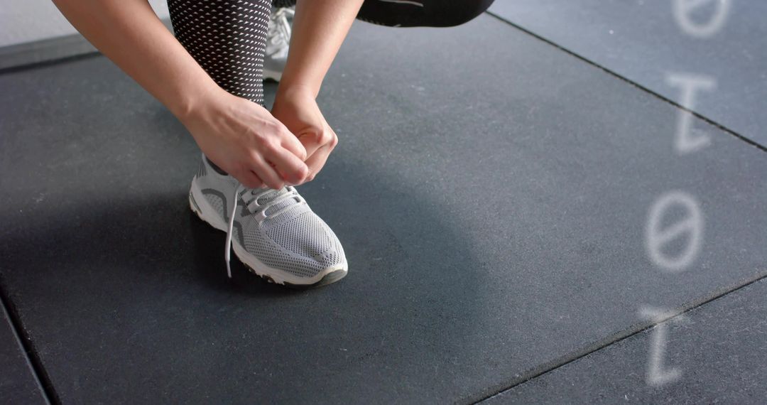 Close-up athlete tying running shoe on gym rubber tiles preparing for training session