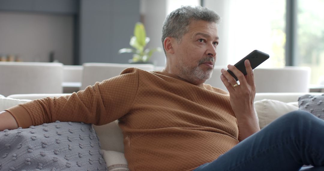 Middle-aged man using smartphone voice command on couch in modern living room - Free Images, Stock Photos and Pictures on Pikwizard.com