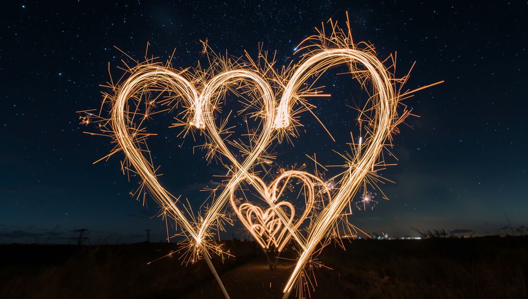 Drawing sparkling heart trails with sparklers under starry sky for romantic celebration