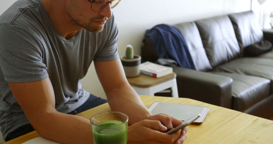 Man Engaged with Smartphone while Drinking Green Smoothie in Casual Setting - Free Images, Stock Photos and Pictures on Pikwizard.com