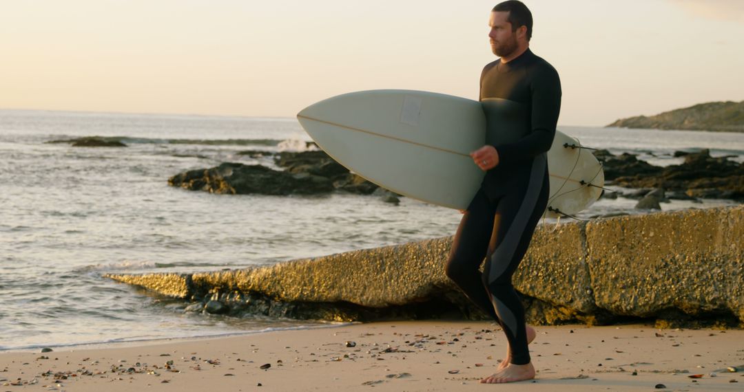 Surfer Carrying Surfboard on Rocky Beach at Sunset - Free Images, Stock Photos and Pictures on Pikwizard.com