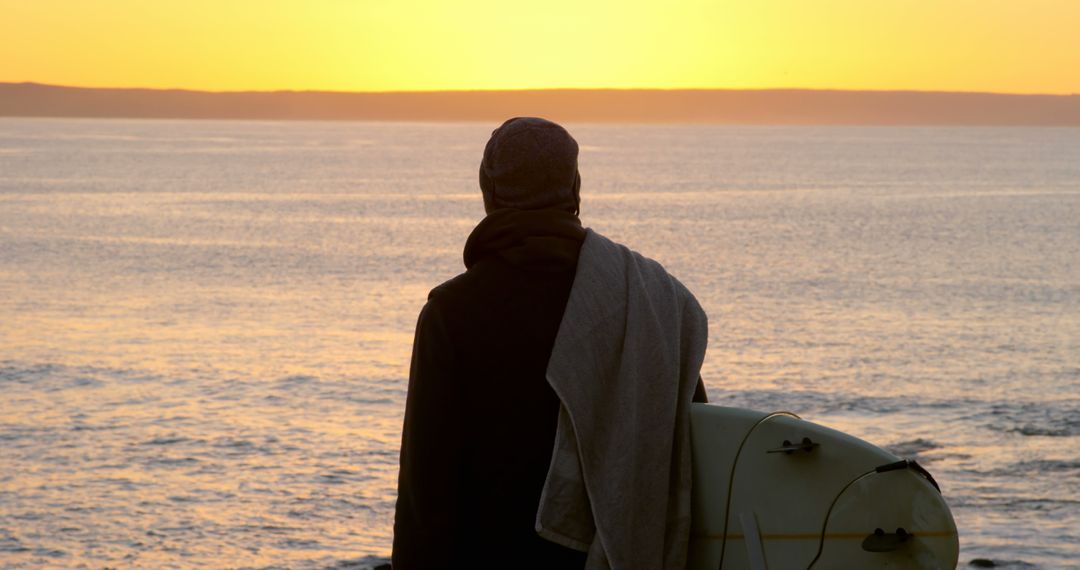 Surfer watching sunset at beach with surfboard - Free Images, Stock Photos and Pictures on Pikwizard.com