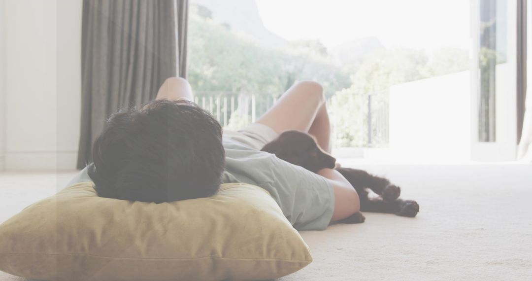 Man lounging on sunlit carpet near patio door with dog and pillow, cozy home relaxation
